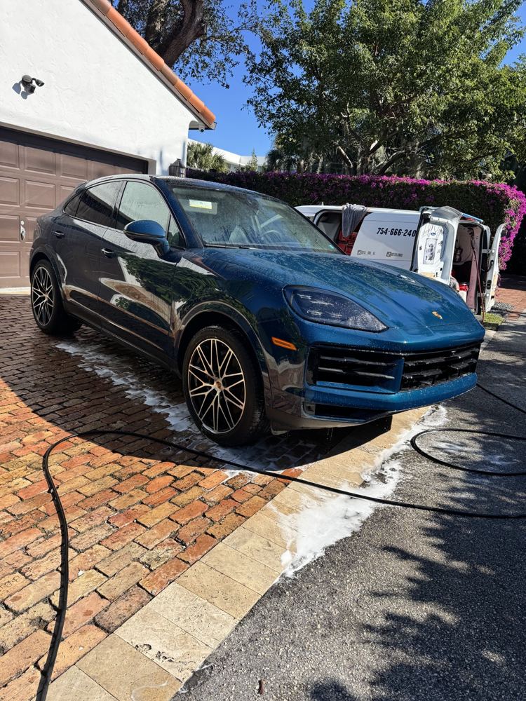 Blue Porsche Cayenne washed in a brick driveway next to the Detail Bros van